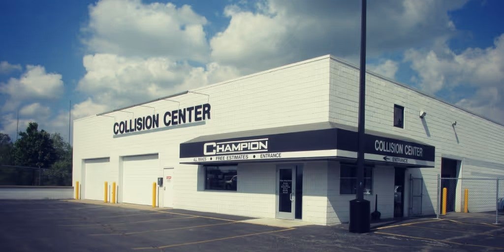 Exterior view of a white collision repair center building with service bays, parking lot, and signage identifying the business