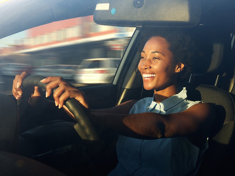 Person seated in the driver's seat of a vehicle with both hands on the steering wheel